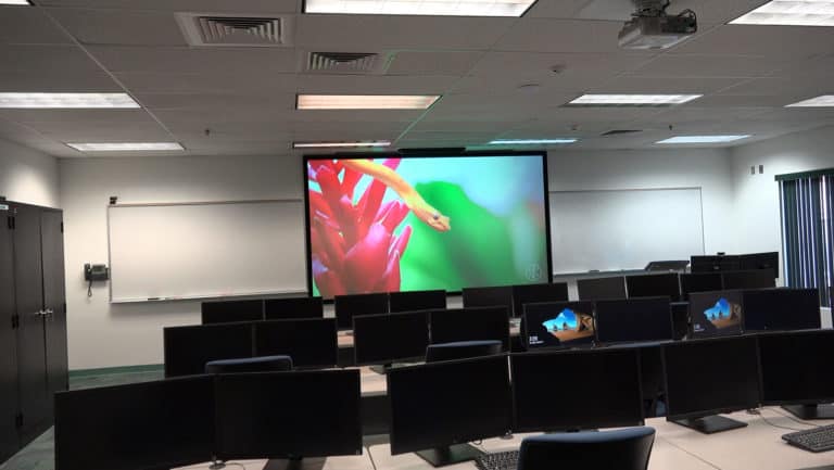 Projection screen in a modern classroom setup with multiple computers and a large display.
