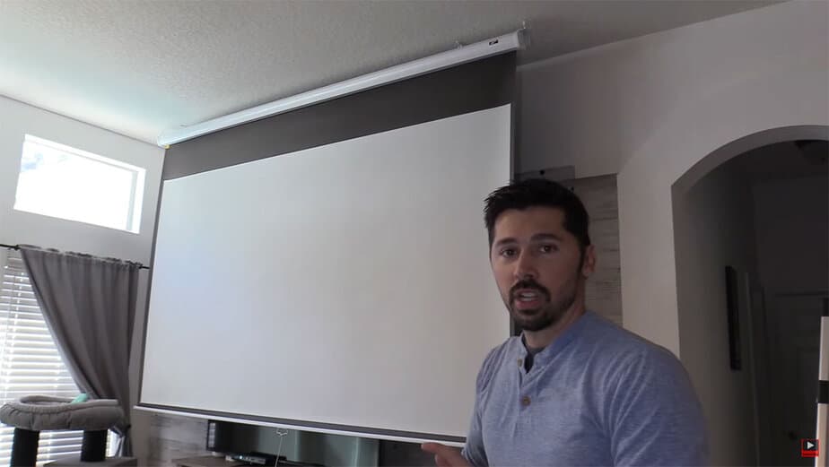 Man demonstrating a large projection screen in a living room.
