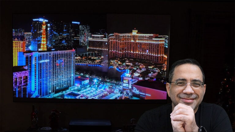 Las Vegas cityscape with bright lights and a smiling man in front of a large projection screen.