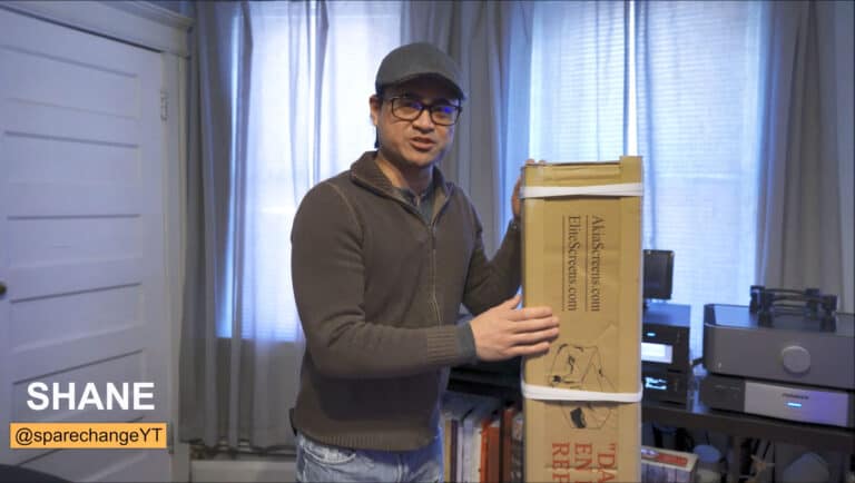 Man setting up a projection screen in a home theater room with audio-visual equipment.