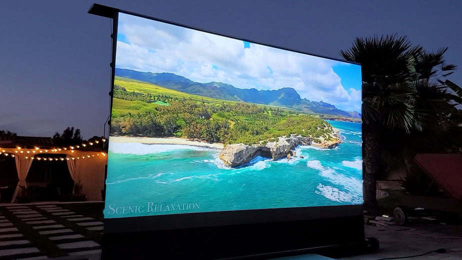 Outdoor projection screen displaying a scenic coastal landscape at dusk.
