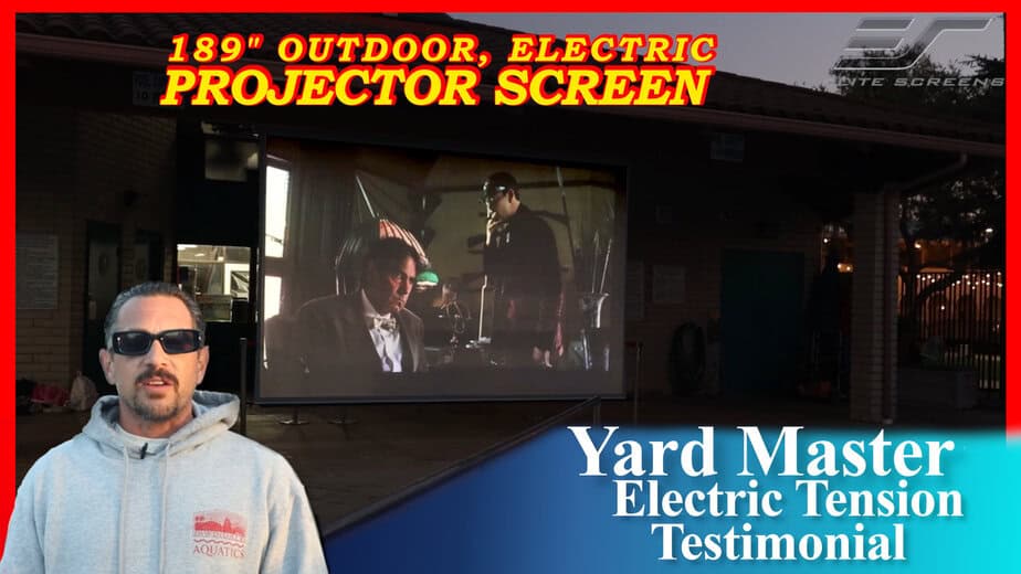 Outdoor electric projector screen displaying a movie at night.
